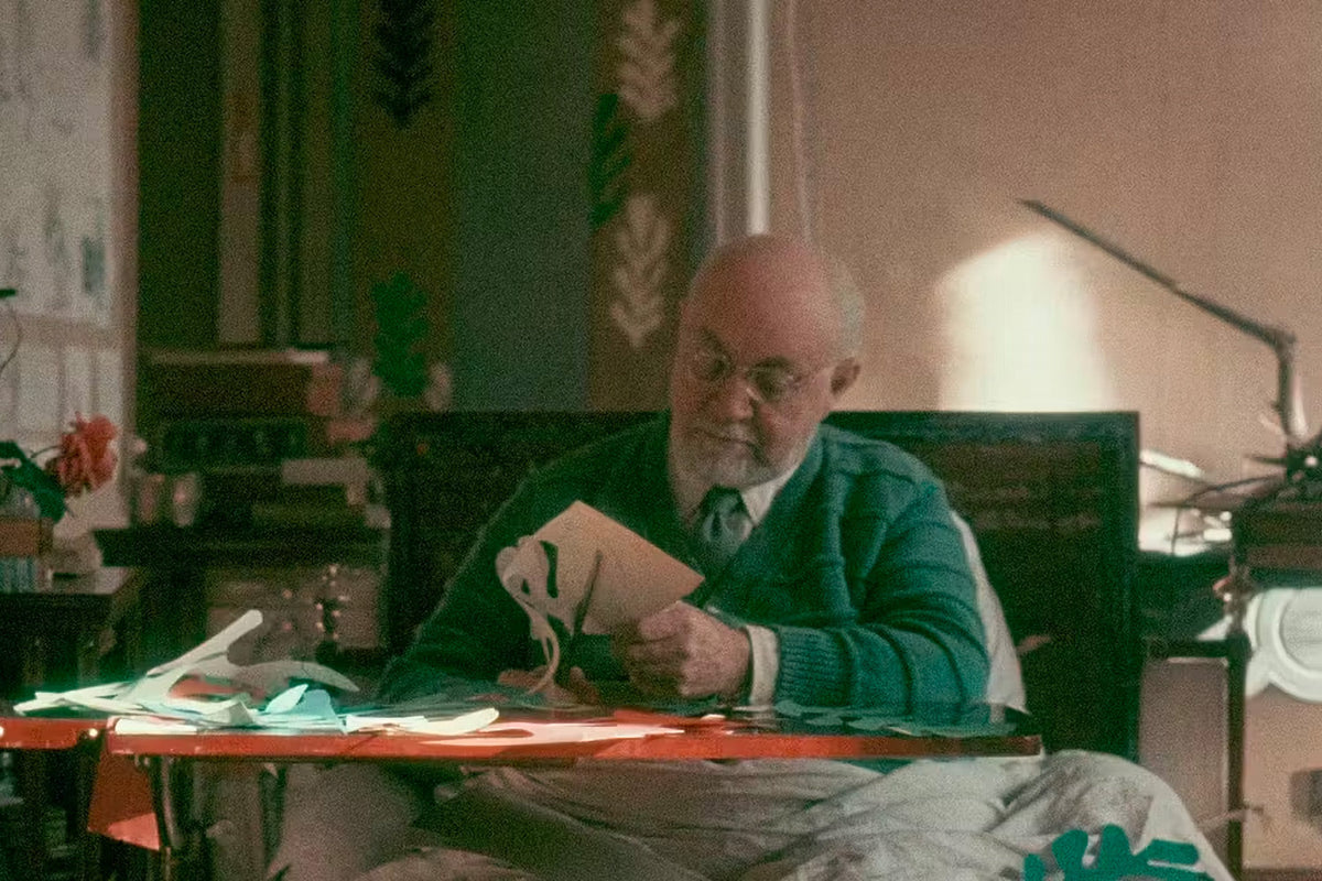 Henri Matisse elämänsä loppuvaiheessa leikkaamassa muotoja maalatusta paperista pöytänsä ääressä